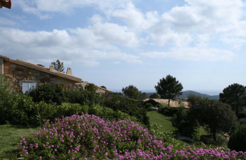 Jardin de l'hôtel Vista D'oro avec fleurs violettes, bâtisse en pierre et vue sur mer surplombant la campagne de Monacia d'Aullène