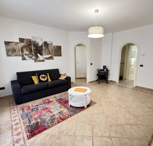 Moderno soggiorno dell'appartamento LA Home Viareggio con divano nero, tappeto colorato, tavolo rotondo bianco e opera d'arte con leone
