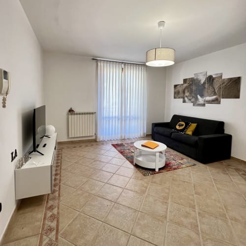 Moderno soggiorno con divano nero, tavolino bianco e TV a schermo piatto nell'appartamento LA Home a Viareggio