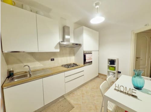 Cucina moderna bianca con piano cottura a gas, lavello e tavolo da pranzo all'appartamento LA Home di Viareggio