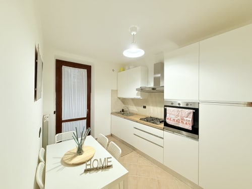 Cucina bianca moderna con zona pranzo nell'appartamento LA Home a Viareggio, con elettrodomestici in acciaio inox e luce naturale