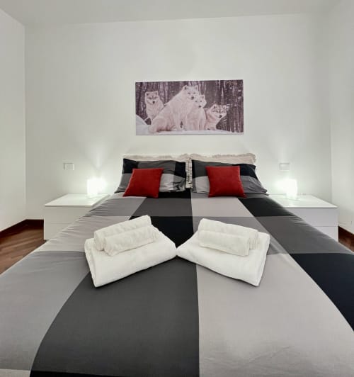 Camera moderna presso LA Home Viareggio con biancheria a righe geometriche, cuscini rossi, asciugamani bianchi e opera raffigurante lupi