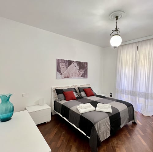 Camera da letto moderna nella LA Home Viareggio con letto a righe, opera d'arte lupo, lampada a sospensione e vista città attraverso le tende.