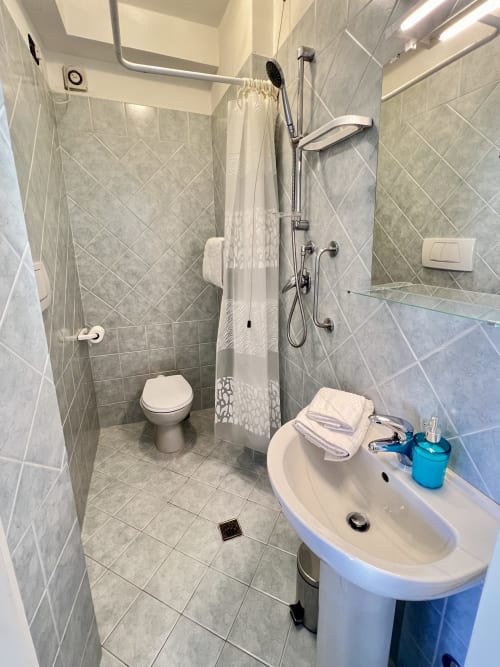 Bagno moderno di LA Home Viareggio con doccia walk-in, WC e lavabo curvo con accessori blu e asciugamani bianchi