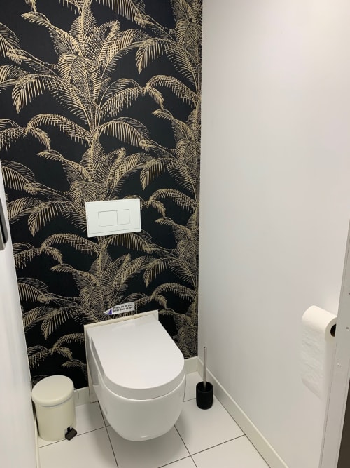 Modern bathroom with white ceramic toilet, black and gold palm leaf wallpaper, and white tile flooring at Villa Ongizatea
