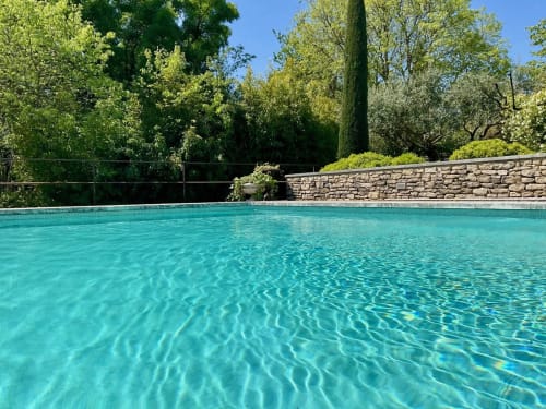 Kristalhelder turquoise zwembad van boutique hotel Provence Km28 in Gordes, omgeven door weelderige groene tuinen en stenen muren