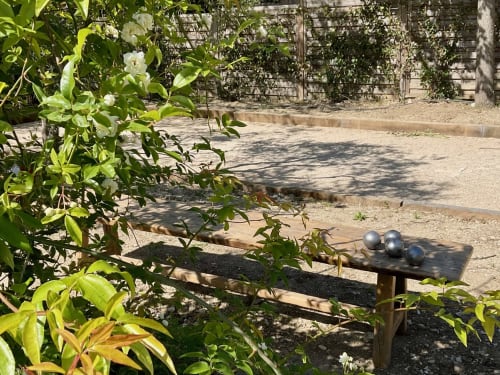 Zonnige tuinpatio van Provence Km28 B&B in Gordes met bloeiende planten, houten bank en jeu de boules