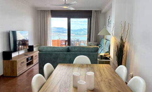 Moderno salón de apartamento con vistas al mar, sofá verde, mesa de comedor de madera y terraza con vistas a la bahía de Baiona