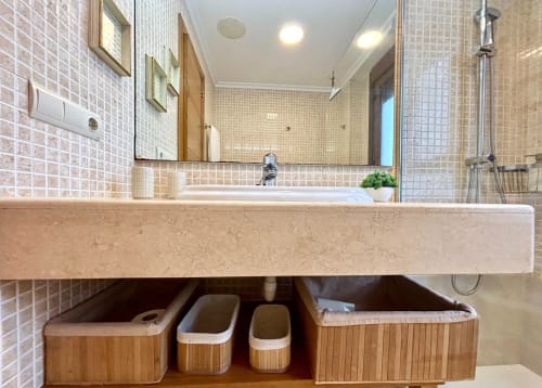 Elegante tocador de baño con paredes de azulejos beige, doble lavamanos, espejo grande y canastos organizadores en A Son do Mar