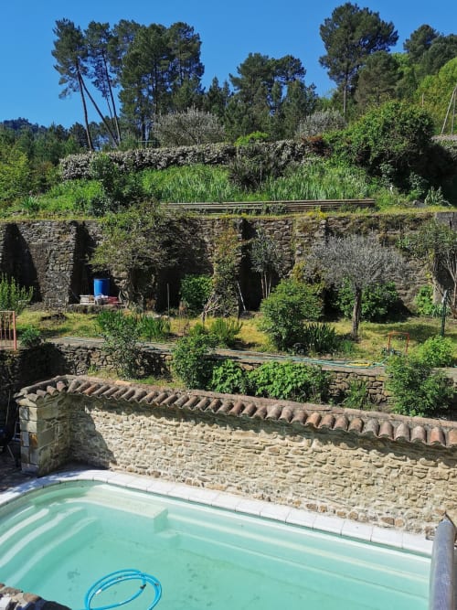 Piscina turchese con muro in pietra alla Chambre d'hôtes Gîte Le Tilleul, giardini terrazzati e alberi a Le Martinet, Francia