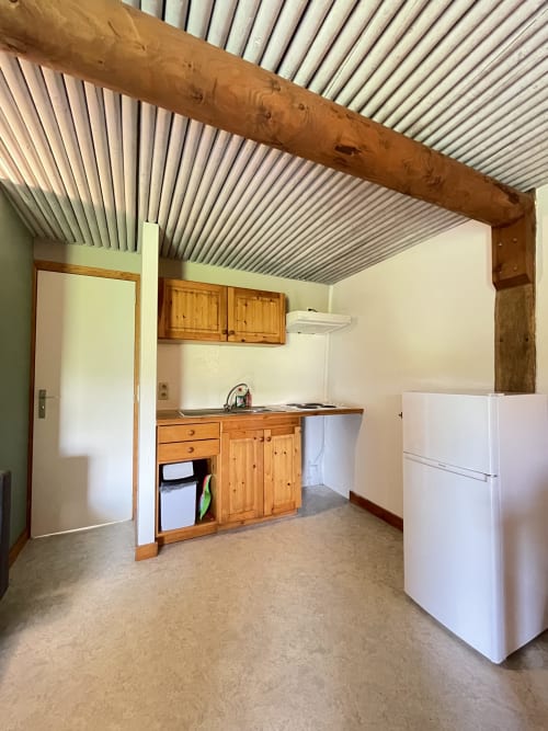 Cuisine spacieuse de l'appartement La Ferme De Werpin à Hotton, avec armoires en bois, réfrigérateur blanc, plafond ondulé et