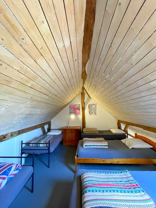Spacieuse chambre mansardée à La Ferme De Werpin avec plafond boisé en pente, plusieurs lits, sol bleu et lumière naturelle