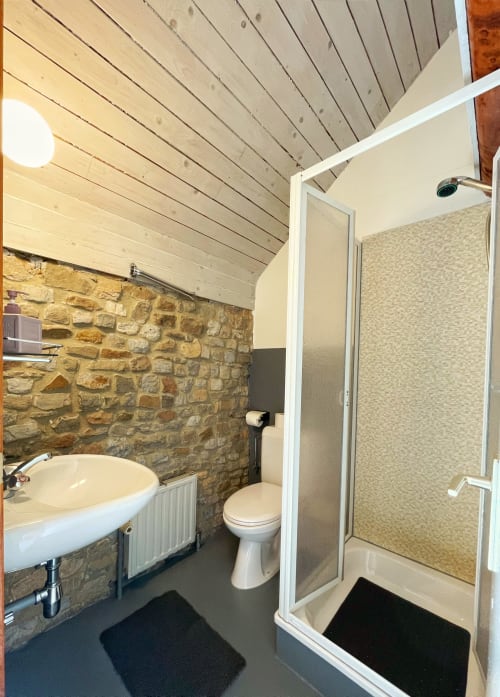 Salle de bain moderne à La Ferme De Werpin avec mur en pierre, lavabo blanc, toilettes et douche