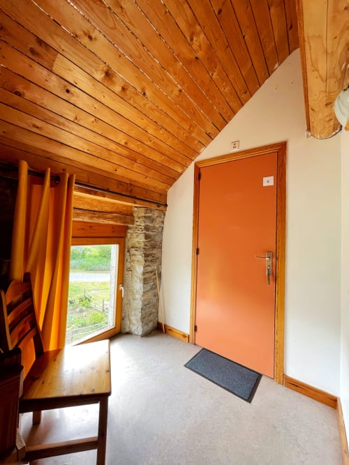 Entrée lumineuse de l'appartement La Ferme De Werpin avec plafond en bois, porte orange et vue sur le jardin à Hotton