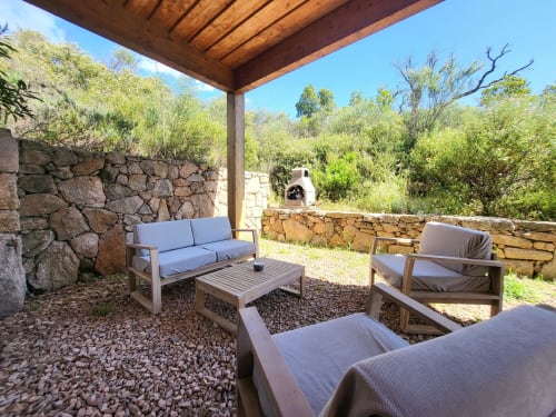 Außenlounge der Villas Lantana in Lecci mit hölzerner Pergola, Steinmauern, bequemen Sitzmöglichkeiten und mediterranem Garten