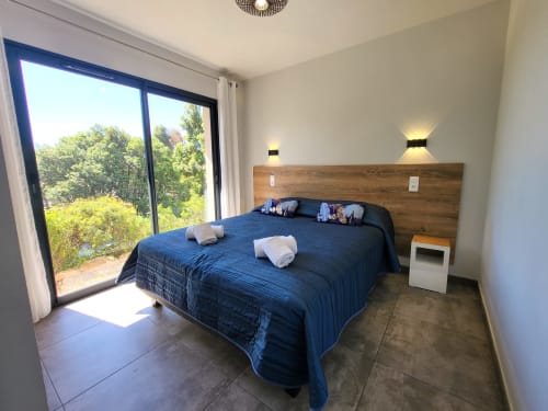 Modern bedroom at Villas Lantana in Lecci with blue bedding, wooden headboard, glass doors opening to garden view