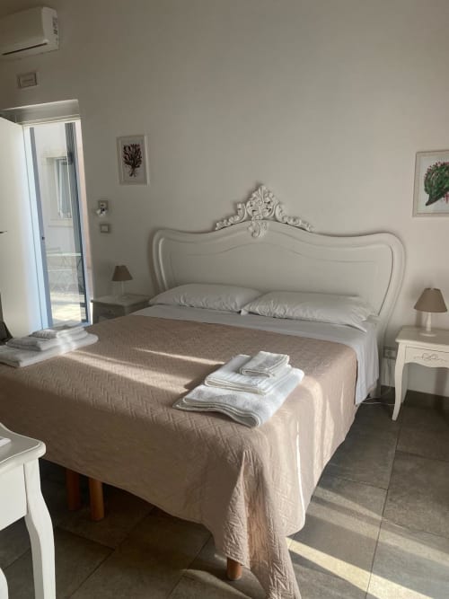 Camera elegante presso Corte Sicula B&B a Siracusa con testiera bianca ornamentale, tonalità neutre e accesso alla terrazza