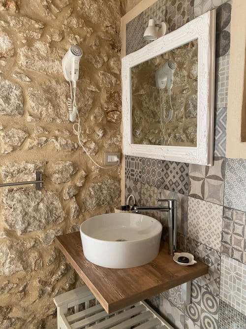 Bagno rustico nella Corte Sicula B&B Siracusa con lavabo in ceramica bianca su piano in legno, muri in pietra e piastrelle decorate