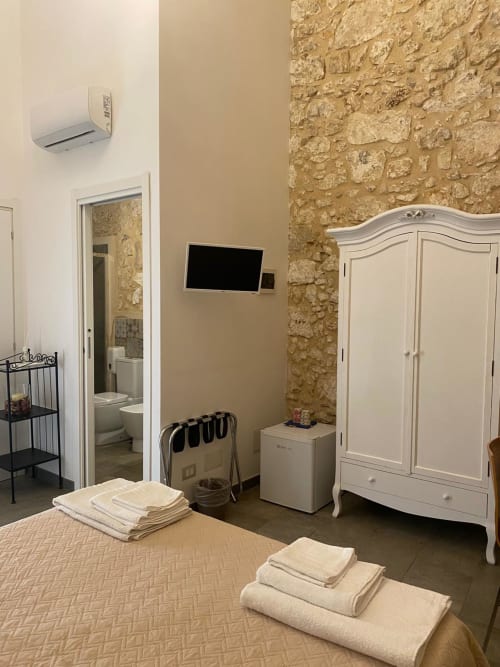 Camera da letto di Corte Sicula a Siracusa con muri in pietra, armadio bianco, TV e biancheria fresca