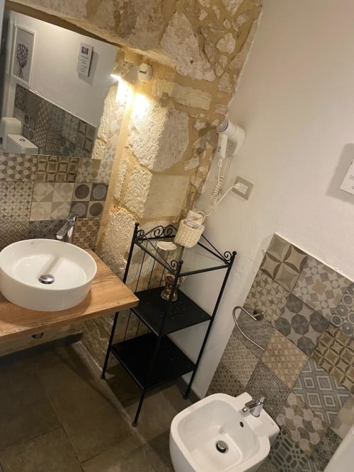 Bagno elegante presso la Corte Sicula B&B di Siracusa con lavabo rotondo bianco, piastrelle decorate e muri in pietra