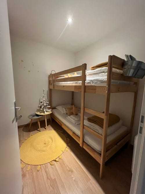 Chambre douillette avec lits superposés à Couleurs Montagne à Valloire, mobilier en bois, tapis rond jaune et vue montagne