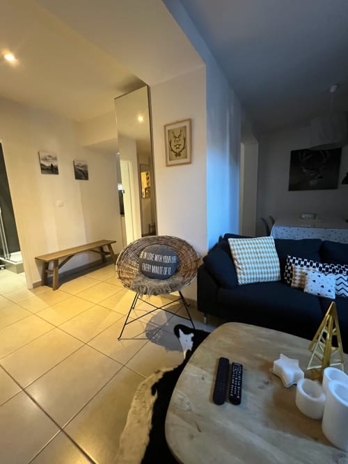 Appartement Couleurs Montagne à Valloire avec salon moderne, fauteuil en rotin, canapé noir et table à manger en bois