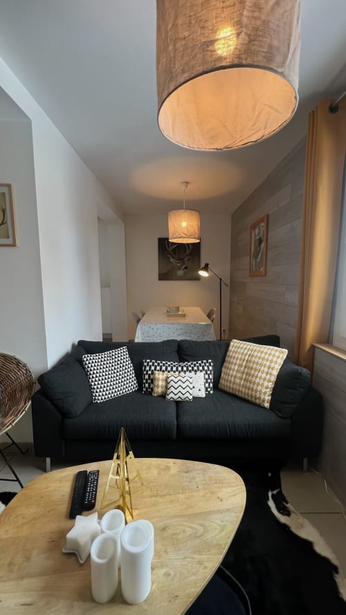 Espace salon contemporain dans l'appartement Jaune Génépi à Couleurs Montagne, Valloire avec canapé noir, table en bois et suspension