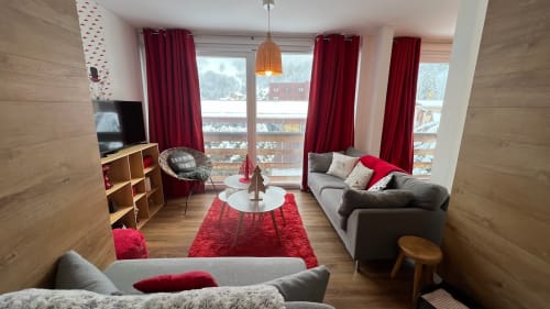 Salon cosy d'appartement montagnard avec accents rouges, canapés gris, parquets et vue sur balcon à Couleurs Montagne