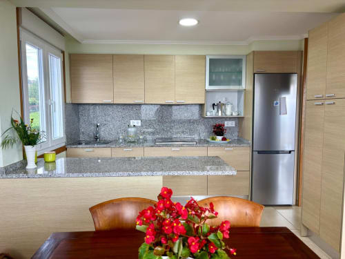 Cocina moderna con muebles de madera clara, encimeras de granito, electrodomésticos de acero inoxidable y zona de comedor en Laranxeira