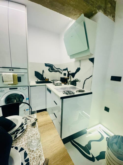 Moderno apartamento cocina-lavandería en Mérida con gabinetes blancos, acentos negros y lavadora-secadora integrada.
