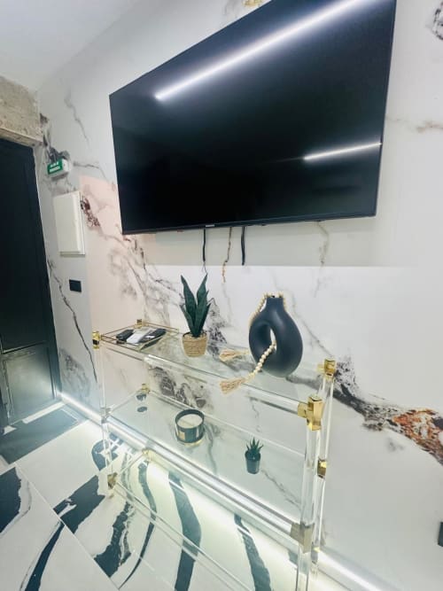 Departamento moderno en Mérida con paredes de mármol, TV en pared, repisas de vidrio con plantas y objetos decorativos, y detalles de acento
