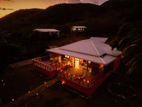Boutique lodge rojo al atardecer, iluminado con luces cálidas, techo de metal, terraza de madera, rodeado de palmeras en San Andrés