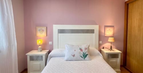Acogedora habitación con paredes rosa, cabecero blanco, almohada floral, lámparas de noche y vistas al mar en la casa en entorno rural Laranxeira de Nigrán