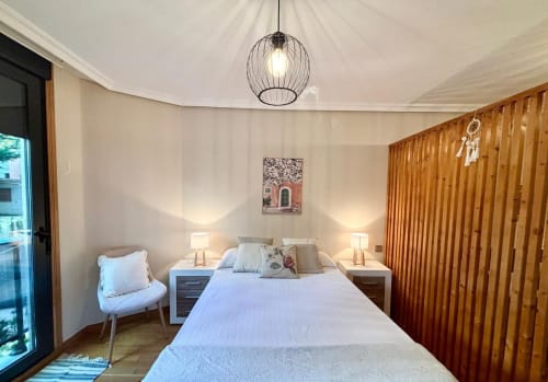 Dormitorio moderno en apartamento Nidiño de Baiona con cama confortable, armario de madera, lámpara colgante y acceso a vistas de piscina