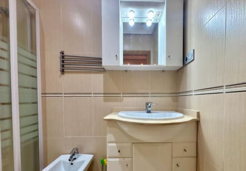 Baño moderno con lavabo redondo, espejo iluminado y paredes de azulejos crema en el apartamento Nidiño, Baiona