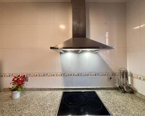 Cocina moderna con campana extractora de acero inoxidable, encimera de granito y azulejos decorativos en el apartamento de Baiona
