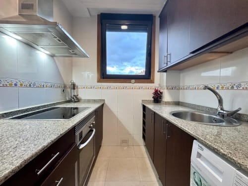 Cocina moderna del apartamento Nidiño en Baiona con encimeras de granito, muebles oscuros, fregaderos de acero inoxidable y vistas por ventana
