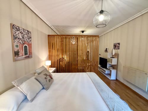 Dormitorio moderno en apartamento de Baiona con cama queen size, persianas de madera, lámpara colgante, escritorio con TV y paredes blancas