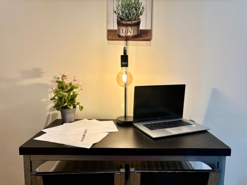 Espacio de trabajo moderno en apartamento Holibai de Baiona con portátil, lámpara de escritorio, flores en maceta y decoración de plantas en pared