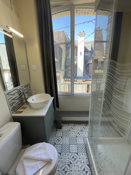 Modern bathroom at Hotel Le Trouville with city views of Trouville sur Mer's rooftops through glass doors