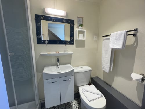 Modern bathroom at Hotel Le Trouville with white vanity, mirror, toilet, and shower in Trouville sur Mer
