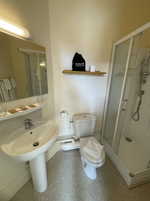 Modern bathroom at Hotel Le Trouville featuring pedestal sink, toilet, and glass shower enclosure with white fixtures