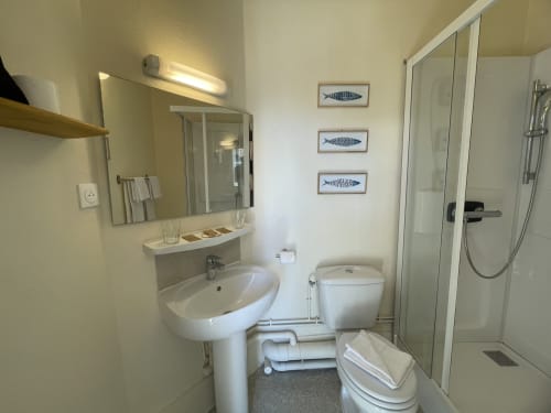 Clean modern bathroom at Hotel Le Trouville with pedestal sink, toilet, shower, and fish artwork