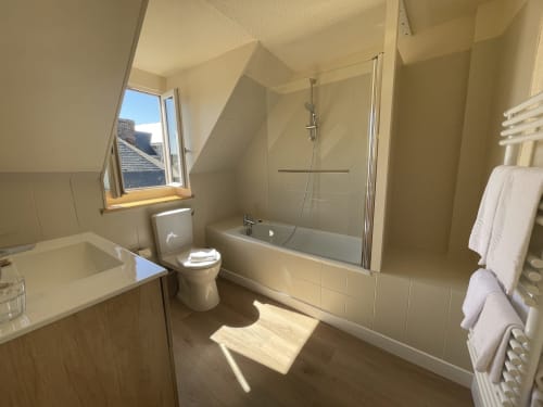Modern attic bathroom at Hotel Le Trouville with bathtub, shower, toilet, and skylight window overlooking city