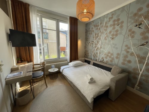 Modern hotel room at Le Trouville with bed, TV, desk, patterned wallpaper, and city view from window