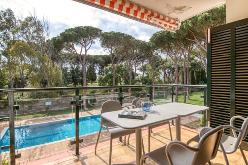 Palafrugell apartment terrace with dining table, chairs, pool view, and pine forest backdrop