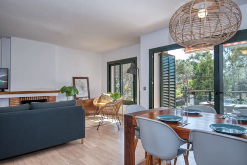 Modern apartment dining area with wooden table, wicker pendant lamp, sea view balcony, and contemporary furnishings in