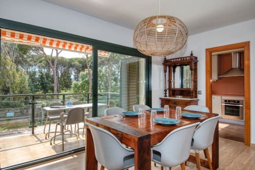 Modern dining room with wooden table, sea view balcony, and kitchen entrance at Canadell apartment in Palafrugell
