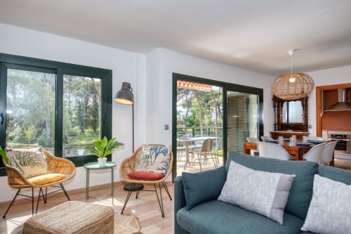 Modern apartment living room in Palafrugell with garden views, wicker chairs, teal sofa, and access to terrace with pool area