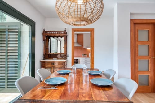 Modern dining room in Palafrugell apartment with wooden table, blue plates, woven pendant light, and garden views